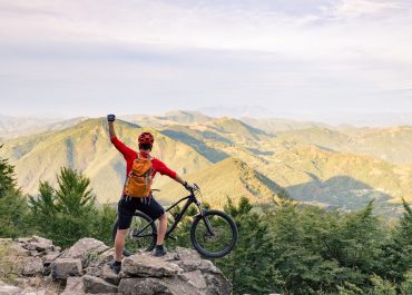 Mountain biker success, looking at view on bike trail in autumn mountains. Celebrating beautiful inspirational landscape. Successful happy rider on rocks. Sport adventure motivation and inspiration.
