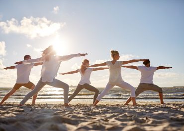 fitness, sport, yoga and healthy lifestyle concept - group of people making warrior pose on beach